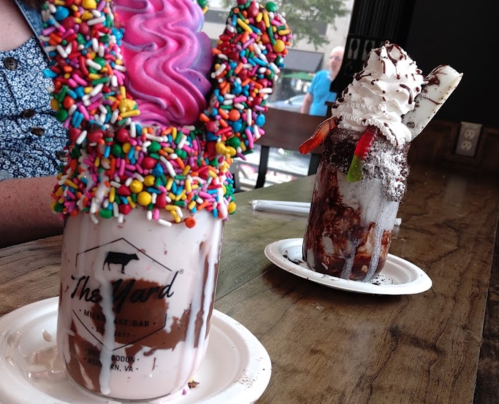 Two colorful milkshakes topped with whipped cream, sprinkles, and candy, served in mason jars on a wooden table.