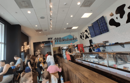 A busy milkshake shop with customers enjoying treats and a colorful menu displayed on the wall.
