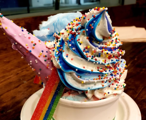 A colorful ice cream sundae topped with blue and white swirls, rainbow sprinkles, and cotton candy.