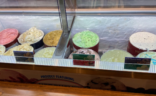 A display of various ice cream flavors in tubs, including pink, gold, green, and black-and-white varieties.