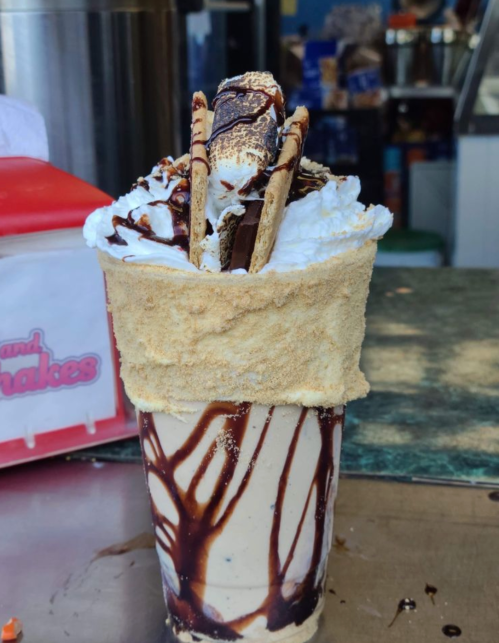 A tall dessert cup filled with ice cream, topped with whipped cream, chocolate syrup, and graham cracker pieces.