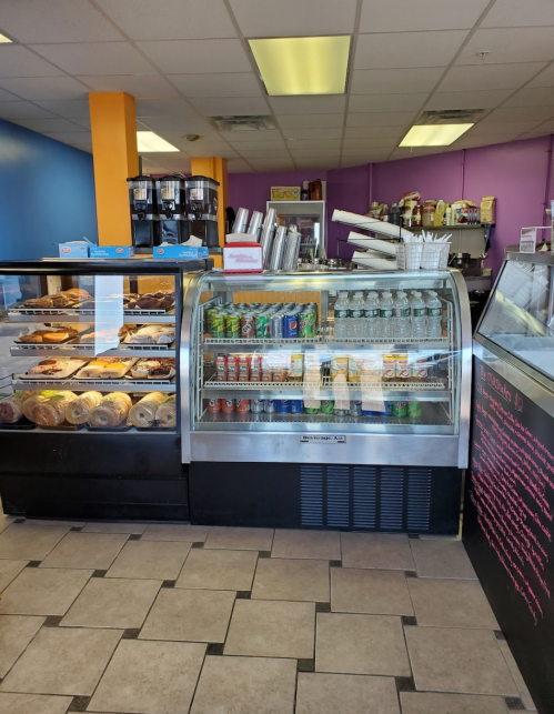 A colorful café display featuring a glass case with pastries and a cooler stocked with drinks.