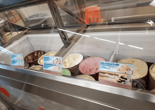 A display of various ice cream flavors in tubs, with flavor labels visible in a shop setting.