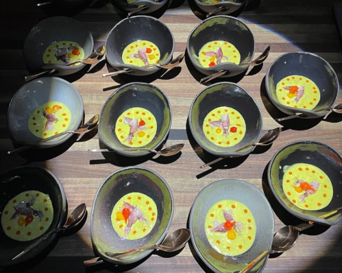 Aerial view of multiple bowls with a yellow dish, garnished with red dots and small pieces of meat, on a wooden surface.