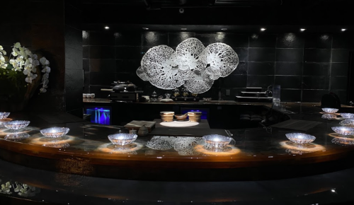 A modern restaurant interior featuring a sleek counter with illuminated bowls and a decorative wall art piece.