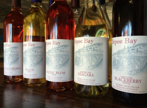 Five bottles of wine with labels featuring illustrations and names: Cranberry, Peach, Pacific Plum, American Niagara, and Oregon Blackberry.