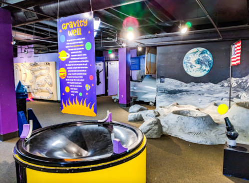 Interactive science exhibit featuring a gravity well, space-themed decor, and a lunar landscape backdrop.