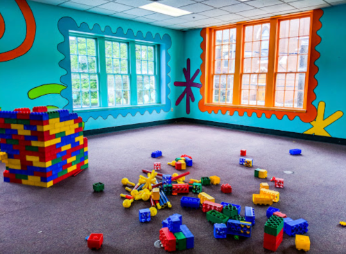 Colorful playroom with vibrant wall murals, scattered building blocks on the floor, and a block tower in the corner.