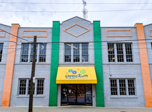 Colorful building exterior with "Explorium" sign and large windows, featuring orange, green, and gray paint.