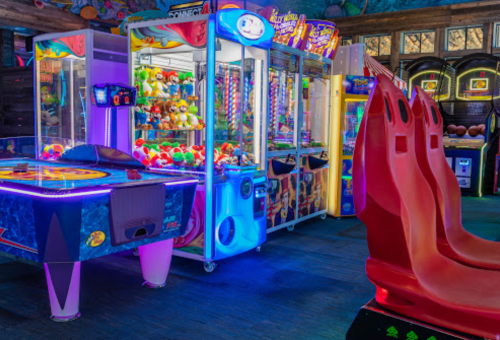 A vibrant arcade scene featuring claw machines, colorful plush toys, and red arcade seating under neon lights.