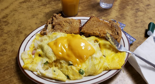 A plate of cheesy omelette with vegetables, served with two slices of toast and a glass of orange juice.