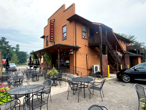 A two-story orange building with outdoor seating and a sign reading "Neithers," surrounded by greenery.