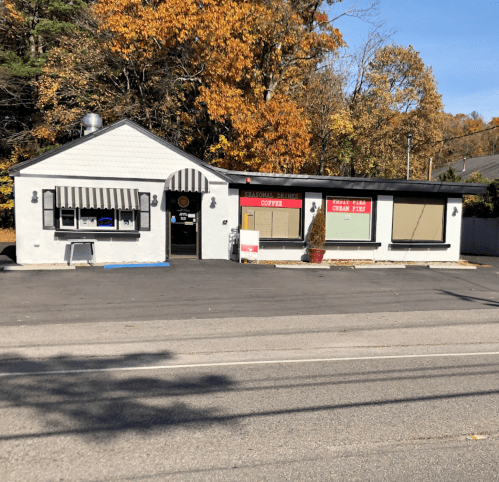 A small, gray building with a striped awning, featuring signs for coffee and cream pies, surrounded by autumn trees.