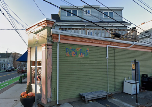 A green building with a sign reading "Pets & Pies," featuring outdoor seating and power lines overhead.