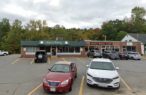 A bakery and a bagel café in a parking lot, with several cars parked outside and trees in the background.