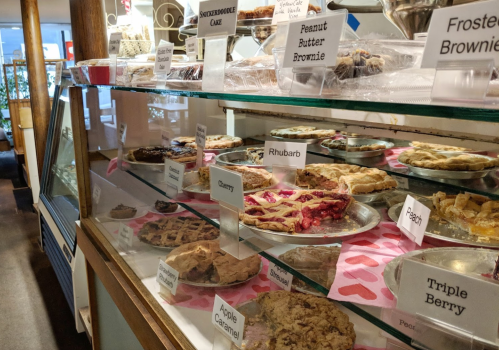 A display case filled with various pies and brownies, labeled with names like cherry, peach, and peanut butter brownie.