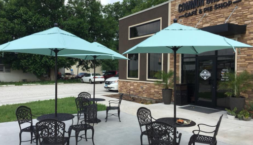 Outdoor seating area with teal umbrellas and black chairs in front of a café and pie shop.