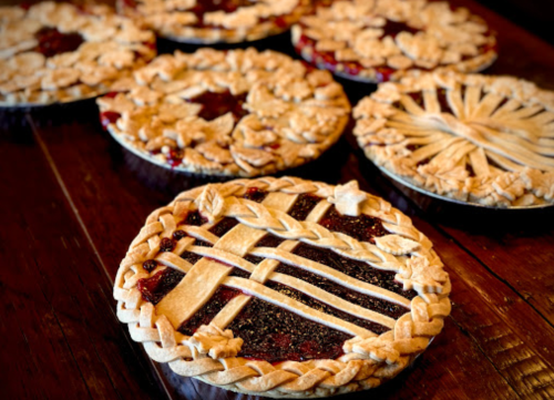 A variety of beautifully decorated fruit pies with intricate crust designs on a wooden table.