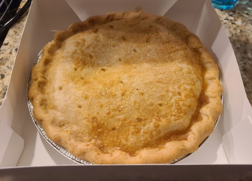 A freshly baked pie in a silver tin, resting in a white box on a granite countertop.
