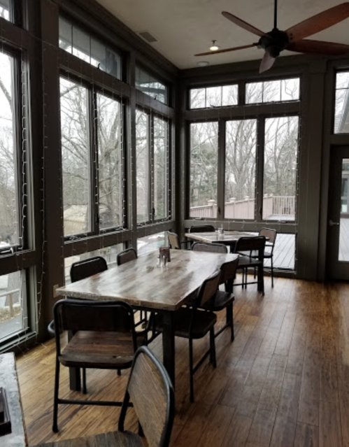 A cozy dining area with wooden tables and chairs, surrounded by large windows overlooking a wooded view.