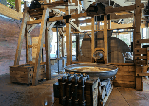 A wooden structure with large wheels and a basin, resembling an old-fashioned water mill or mining equipment.