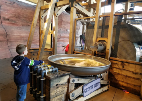 A child interacts with a water feature at a museum, observing water flowing in a large metal basin.