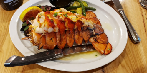 A plate of grilled lobster tail with lemon, garnished with herbs and served with green vegetables.