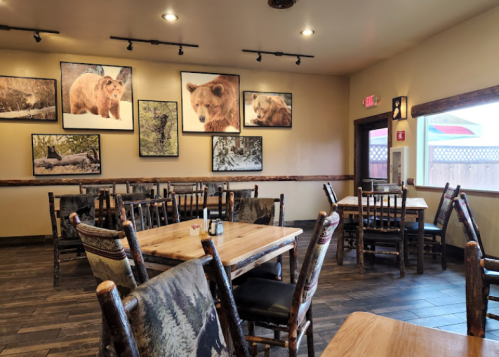 Cozy restaurant interior with wooden tables, chairs, and bear-themed artwork on the walls. Natural light from a window.