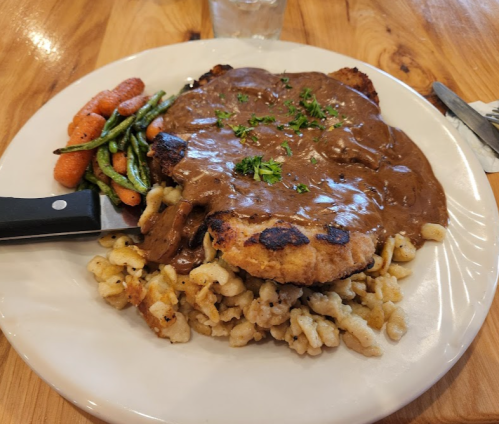 A plate of chicken with gravy, served over pasta, alongside green beans and carrots on a wooden table.