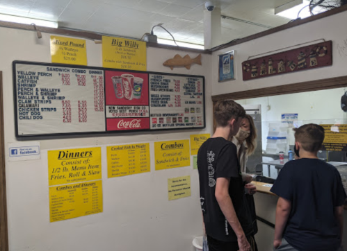 A menu board with food options and prices, featuring sandwiches, dinners, and combos, in a casual dining setting.