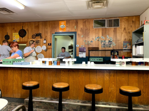A diner interior with a wooden wall, a counter with stools, and staff preparing food in the background.