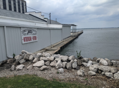 A gray building by the water with a dock and a sign reading "New Sandusky Fish Company" in a cloudy sky.