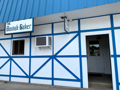 Exterior of a bakery with a blue and white facade, featuring a sign that reads "The Danish Baker" and an entrance door.