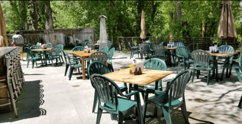 Outdoor dining area with green chairs and wooden tables, surrounded by trees and a sunny atmosphere.