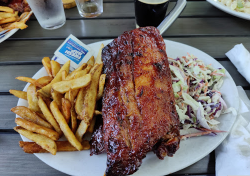 A plate of BBQ ribs with coleslaw and fries, accompanied by a small packet of sauce.