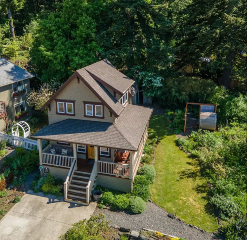 Aerial view of a charming two-story house surrounded by greenery and a well-maintained garden.