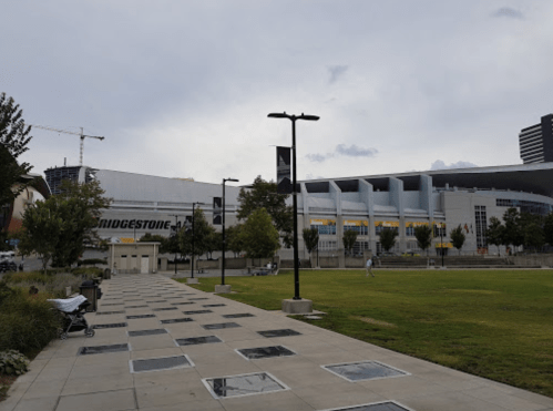 View of Bridgestone Arena from a nearby park, featuring trees, pathways, and a cloudy sky.