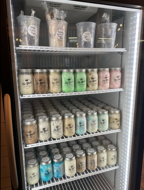 A refrigerator filled with jars of colorful candles, neatly arranged on shelves.