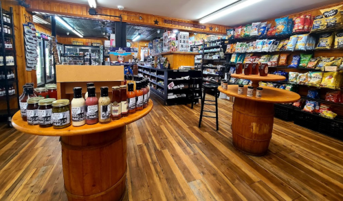 Interior of a store featuring wooden displays with sauces and snacks on shelves, and a warm, inviting atmosphere.
