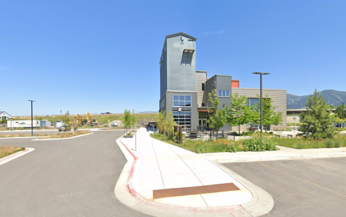 Modern building with a tower, surrounded by greenery and a clear blue sky, located at a street intersection.