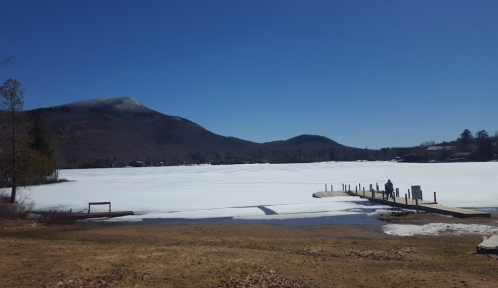 A frozen lake under a clear blue sky, with mountains in the background and a person walking on a dock.