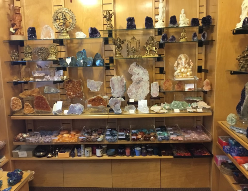 A display of various crystals and minerals on shelves, featuring sculptures and decorative items in a shop setting.