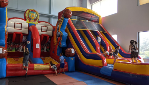 Children playing on colorful inflatable bounce houses and slides in a bright indoor play area.
