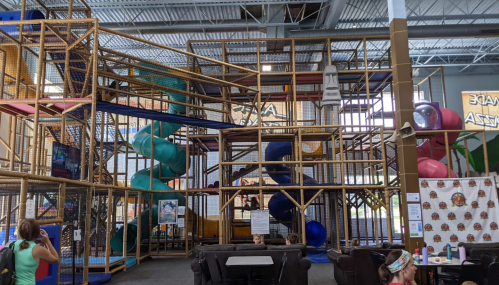 A colorful indoor play structure with slides and climbing areas, filled with children playing and exploring.