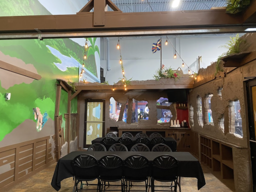 A rustic event space with a long table, string lights, and a mural of nature on the walls.