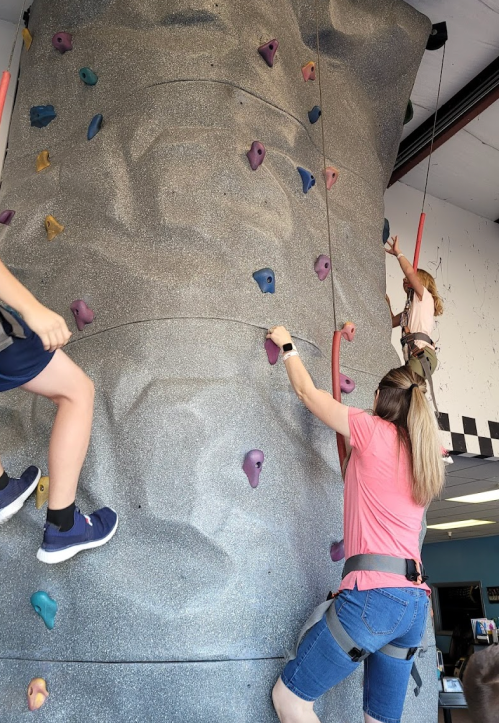 Two climbers ascend a rock wall indoors, one adult and one child, both secured with harnesses.