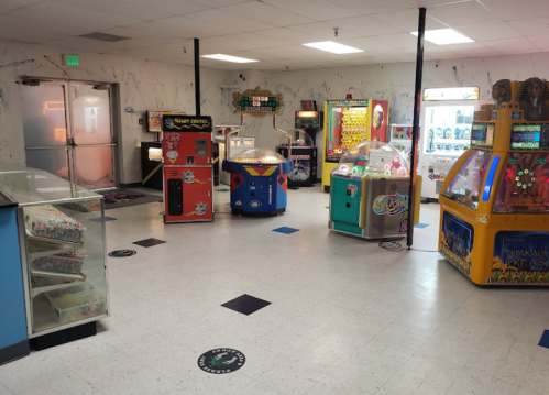 A spacious arcade with various vintage game machines and colorful prize booths in a well-lit room.