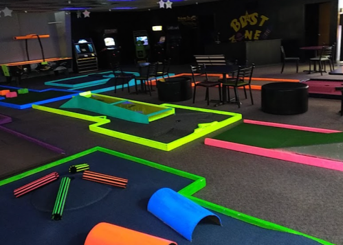 A brightly colored mini-golf course with neon obstacles and seating in a recreational space.