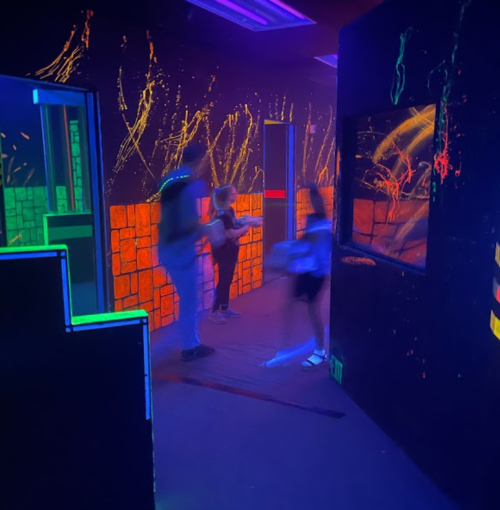 A brightly lit room with neon colors, featuring people moving through a maze-like space with glowing walls.