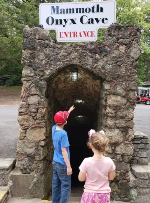Two children stand at the entrance of Mammoth Onyx Cave, pointing into the dark tunnel ahead.